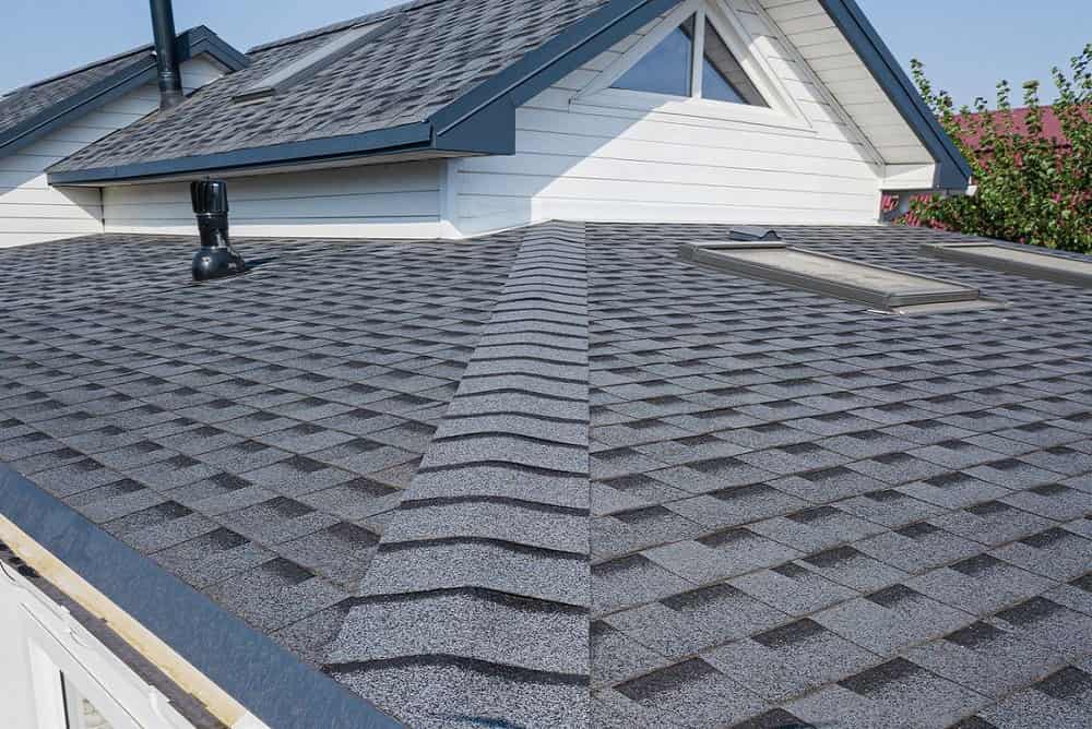 Gray asphalt shingle roof with vent and skylight on residential home, showcasing roofing services and new roof installation.